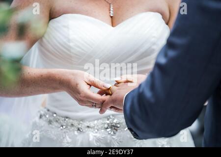 Primo piano di uno sposo che tiene la mano come sposa in abito bianco durante la cerimonia di nozze mettendo l'anello sul dito Mentre dicevo voti e io sigilli il matrimonio Foto Stock