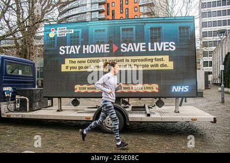 PUTNEY LONDON, REGNO UNITO. 4 Feb 2021. Un jogger passa accanto a un grande segno digtial di informazioni da NHS Inghilterra in Putney High Street come parte della campagna del governo NHS per mantenere Londra sicuro dopo che una nuova variante Sud Africa Covid-19 è stato scoperto senza collegamenti al Sud Africa in otto codici postali in Inghilterra e il Credito Sud Est: amer Ghazzal/Alamy Live News Foto Stock