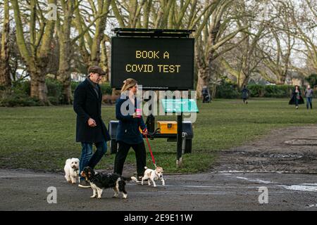 PUTNEY LONDON, REGNO UNITO. 4 Feb 2021. Persone che camminano i loro cani oltre un grande segno digziale di informazione nel Parco del Vescovo, Putney esortando i membri del pubblico a prenotare un test per i sintomi covidi. Alle persone in Inghilterra e nel Sud-est sono stati offerti porta a porta test Covid-19 in otto codici postali dopo che una nuova variante sudafricana Covid-19 è stata scoperta senza alcun collegamento con il Sud Africa. Credit: amer Ghazzal/Alamy Live News Foto Stock