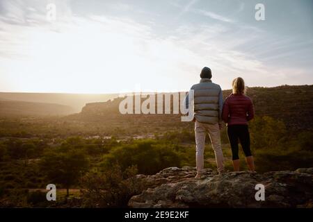 Vista posteriore del giovane uomo e della donna in piedi in montagna scogliera che guarda all'alba Foto Stock
