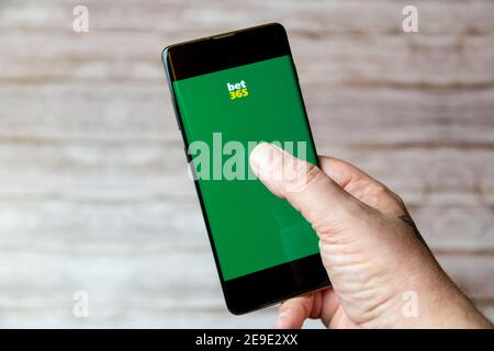 Una mano che tiene un telefono cellulare o un telefono cellulare con L'app di scommesse o scommesse Bet 365 sullo schermo Foto Stock