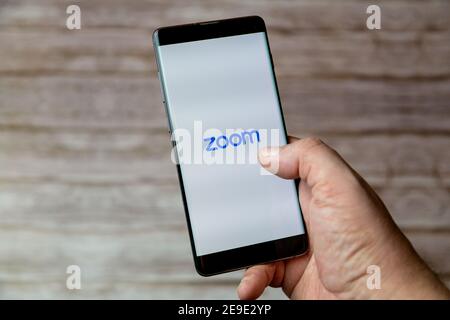 Una mano che tiene un telefono cellulare o cellulare con L'app Zoom Calling sullo schermo Foto Stock