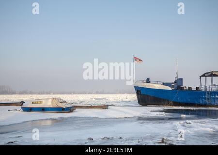 Nave da carico e una barca intrappolata sul Danubio congelato durante l'inverno 2017, a Zemun, Belgrado, Serbia con ghiaccio che fuoriesce dall'acqua. Quest'inverno è stato parti Foto Stock