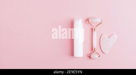 Kit per la cura del viso, massaggiatore a rullo, raschietto al quarzo gua sha, siero cosmetico o olio su sfondo rosa pastello. Sollevamento e tonificazione fitness per il viso a h. Foto Stock