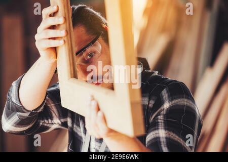 Un giovane falegname maschile che lavora nel complesso equivale ad una barra di legno con una fresatrice in officina, sullo sfondo in legno Foto Stock