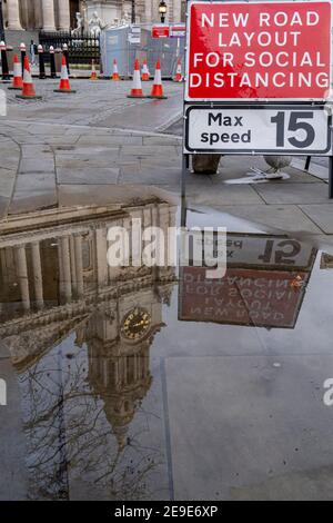 Il riflesso della Cattedrale di San Paolo è visto in una pozza sul marciapiede, accanto a un segnale stradale che avverte i conducenti di un restringimento della strada, ampliato per i pedoni che si allontanano sociali durante il terzo blocco della pandemia di Coronavirus, nella 'City of London', il quartiere finanziario della capitale, Aka The Square Mile, il 2 febbraio 2021, a Londra, Inghilterra. Foto Stock