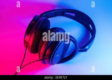 Eleganti cuffie wireless nere illuminate con coloratissima luce al neon su sfondo astratto isolato. Concetto di tecnologia moderna con spazio di copia Foto Stock