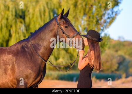 Una ragazza bacia un cavallo tra i raggi del tramonto Foto Stock