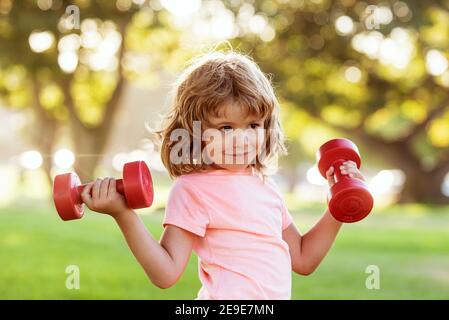 Capretto sportivo con manubri nel parco. Sport per bambini. Ragazzo che si esercita all'aperto. Uno stile di vita attivo e sano. Foto Stock