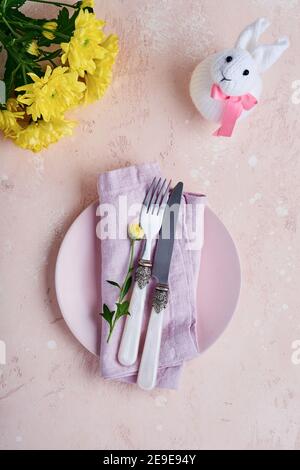 Tavolo di saluto di Pasqua con decorato con crisantemi gialli e simpatico coniglio su sfondo di colore rosa. Vista dall'alto. Spazio per il testo. Foto Stock