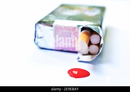 il filtro per sigarette fuoriesce dalla confezione con il sangue che gocciola sfondo bianco Foto Stock