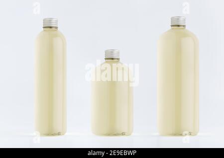 Assortimento di tre bottiglie di plastica alte, basse e spesse con bevanda fresca pallida o olio essenziale cosmetico, mockup di tappo argentato su sfondo bianco, templa Foto Stock