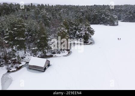 Aviemore, Scozia, Regno Unito. 4 febbraio 2021. Loch VAA è completamente congelato e offre l'opportunità di attraversare a piedi. Un piccolo boathouse è ora icebound e tre Signore del gruppo di nuoto selvaggio InVaa Dookers usano gli assi per rompere il ghiaccio per permettere loro di immergersi nell'acqua ghiacciata per alcuni minuti. PIC; veduta aerea della boathouse sul VAA di Loch congelato. Iain Masterton/Alamy Live News Foto Stock