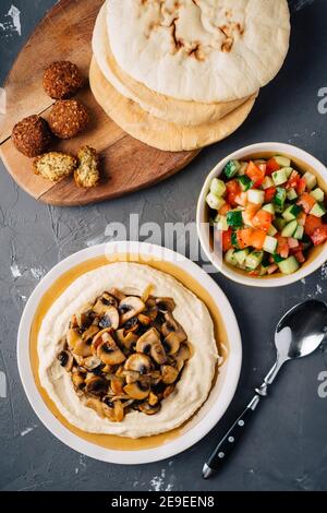 Hummus con funghi fritti, insalata di cetrioli e pomodori, falafel e pita. Sfondo scuro. Vista dall'alto Foto Stock