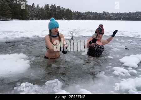 Aviemore, Scozia, Regno Unito. 4 febbraio 2021. Loch VAA è completamente congelato e offre l'opportunità di attraversare a piedi. Un piccolo boathouse è ora icebound e tre Signore del gruppo di nuoto selvaggio InVaa Dookers usano gli assi per rompere il ghiaccio per permettere loro di immergersi nell'acqua ghiacciata per alcuni minuti. PIC; Carolyn Stead e Wendy Cathcart spezzano il ghiaccio in Loch VAA. Iain Masterton/Alamy Live News Foto Stock