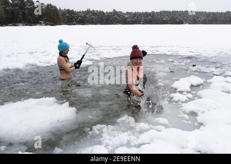 Aviemore, Scozia, Regno Unito. 4 febbraio 2021. Loch VAA è completamente congelato e offre l'opportunità di attraversare a piedi. Un piccolo boathouse è ora icebound e tre Signore del gruppo di nuoto selvaggio InVaa Dookers usano gli assi per rompere il ghiaccio per permettere loro di immergersi nell'acqua ghiacciata per alcuni minuti. PIC; Carolyn Stead e Wendy Cathcart spezzano il ghiaccio in Loch VAA. Iain Masterton/Alamy Live News Foto Stock