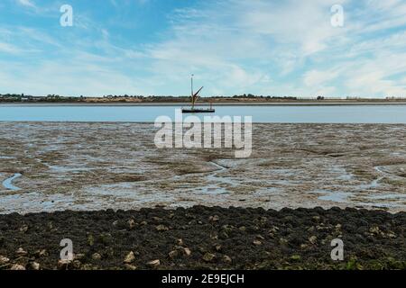 Barca a vela sull'estuario della Swale a bassa marea a Oare vicino a Faversham in Kent, che domina l'isola di Sheppey Foto Stock