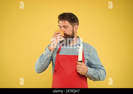 Cucina sana. Preparazione di insalate fresche. Chef professionista nel grembiule rosso. La cucina è il suo hobby. Uomo barbuto in uniforme cuoco. Casalinga sicura preparare il pomodoro. Uomo maturo tenere coltello e verdure. Foto Stock