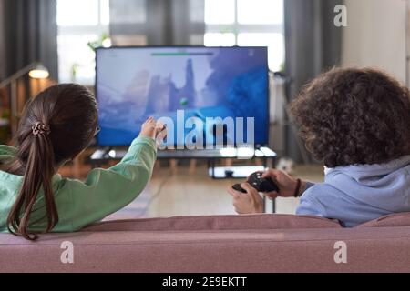 Vista posteriore di due amici seduti sul divano e giocando Videogioco insieme sulla grande TV Foto Stock