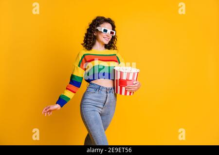 Foto di allegra adorabile giovane bruna capelli donna stand mangiare il film di orologio popcorn indossa occhiali jeans felpa isolati sul giallo sfondo Foto Stock