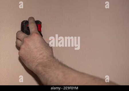 Nella mano del lavoratore, la livella laser brilla con un fascio rosso una linea sulla parete. Foto Stock