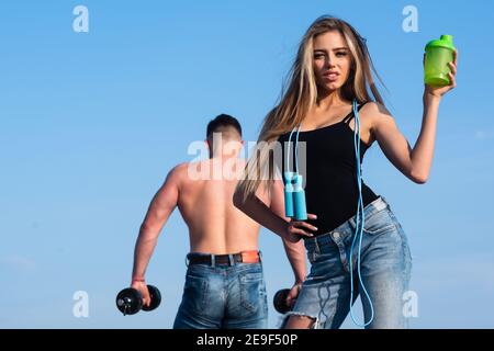 Donna slim fitness trainer con agitatore proteico. Sorridente giovane donna e allenatore di coppia personale. Uomo e ragazza con bottiglia di frullato proteico e saltellando Foto Stock