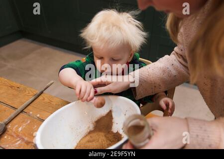 Ragazzo giovane che aiuta la mamma ad aggiungere gli ingredienti in una ciotola in cucina. Foto Stock