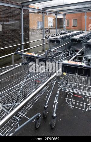 I carrelli per lo shopping del supermercato si trovano in un parcheggio coperto tra tubi in acciaio inox in una giornata piovosa Foto Stock