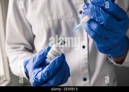 Primo piano medico indossando i guanti blu disegna il vaccino Covid-19 in una siringa, preparandosi per la vaccinazione Shot. Nuovo normale Foto Stock