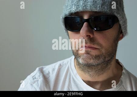 Ritratto di un uomo in occhiali da sole, un cappello invernale e una T-shirt bianca Foto Stock