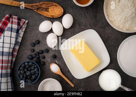 Una visualizzazione degli ingredienti umidi e secchi necessari per preparare muffin ai mirtilli sul banco della cucina Foto Stock