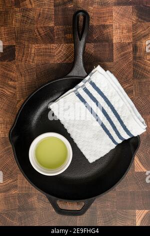 Una padella in ghisa preparata per essere condita, con una tazza di olio di semi di pompelmo e un asciugamano su un tagliere Foto Stock
