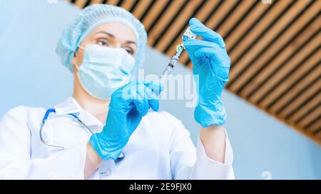 Un medico che indossa una maschera medica protettiva si prepara ad iniettare con il vaccino del coronavirus. Il concetto di trattamento domestico, che chiama il medico a casa. Foto Stock