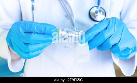 Il medico disimballa una siringa monouso da vicino su sfondo blu. Il concetto di immunizzazione della popolazione e la vaccinazione contro COVID-19 coro Foto Stock