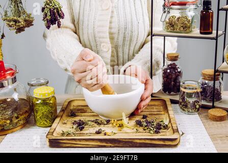 Primo piano vista di erborista donna mescolando varie erbe secche per il tè medicinale tradizionale con mortaio e pestello. Erbe secche in vasi di vetro. Foto Stock