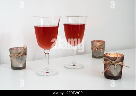 Primo piano di un paio di bicchieri con vino e candele con cuori di legno sul tavolo. Composizione romantica. Sfondo bianco. Foto Stock