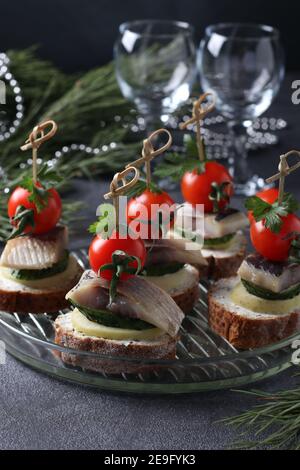 Canape con aringhe salate, cetrioli, patate bollite, pomodori ciliegini e olive nere su crostini di segala su fondo grigio. Formato verticale Foto Stock