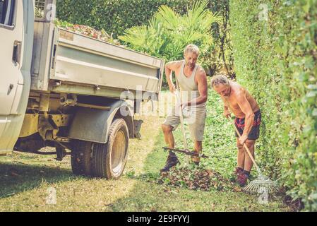 I giardinieri stanno rimuovendo le foglie con i rastrelli nel giardino. Foto Stock