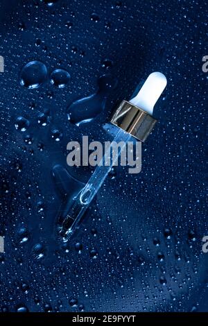 prodotti di bellezza idratanti concetto - sfondo blu classico con medicina contagocce e spruzzi d'acqua intorno ad esso Foto Stock