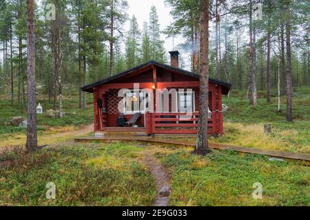 Misterioso cottage in legno rosso a Inari, Lapponia, Finlandia in un giorno di autunno foggy in idilliaca pineta. Cabina solitaria per una tranquilla e rilassante vacanza suomi Foto Stock