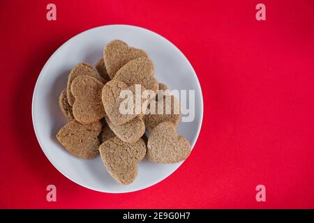 Bistuit a forma di cuore su un piatto bianco su sfondo rosso, vista cenitale con spazio di copia Foto Stock