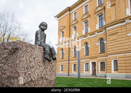 OULU, FINLANDIA - 12 ottobre 2020: Primo piano di una giovane scultura in bronzo del ragazzo di fine seduta di fronte al municipio su granito che sorride al passaggio di Tim Foto Stock