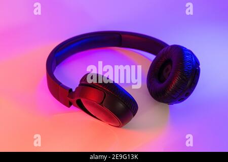 Eleganti cuffie wireless nere illuminate con coloratissima luce al neon su sfondo astratto isolato. Concetto di tecnologia moderna con spazio di copia Foto Stock