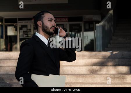 Uomo d'affari giovane ispanico vestito con stile in una chiamata importante lungo le strade della città Foto Stock