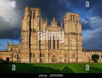 Facciata della Cattedrale di St Andrew di Wells Inghilterra bagnata Luce del sole dorata in UN giorno estivo di sole con alcuni Nuvole scure nel cielo Foto Stock