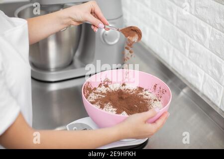 Primo piano di mani di chef professionista, versando il cacao in polvere nella ciotola con farina bianca. Preparazione di macaron, torte e dessert Foto Stock