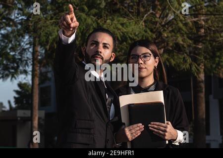 Giovane ispanico che mostra qualcosa in lontananza al suo partner commerciale femminile Foto Stock