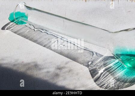 Closeup di un pallone da laboratorio con reagente turchese e un ombra su una superficie bianca grunge Foto Stock
