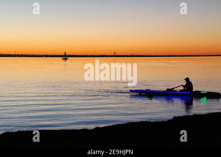 Un uomo solista pagaia un kayak vicino alla riva del lago Hefner al tramonto in una serata invernale. Foto Stock