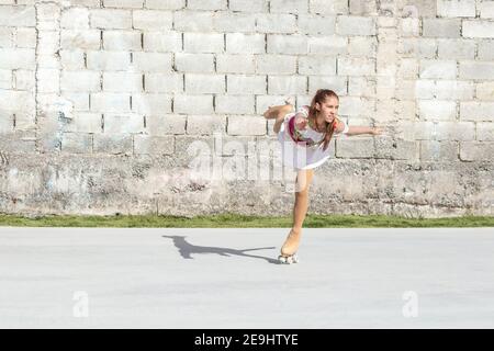 Ragazza adolescente che fa una figura di pattinaggio di figura di rullo di figura che gira su una gamba sulla pista. Foto Stock